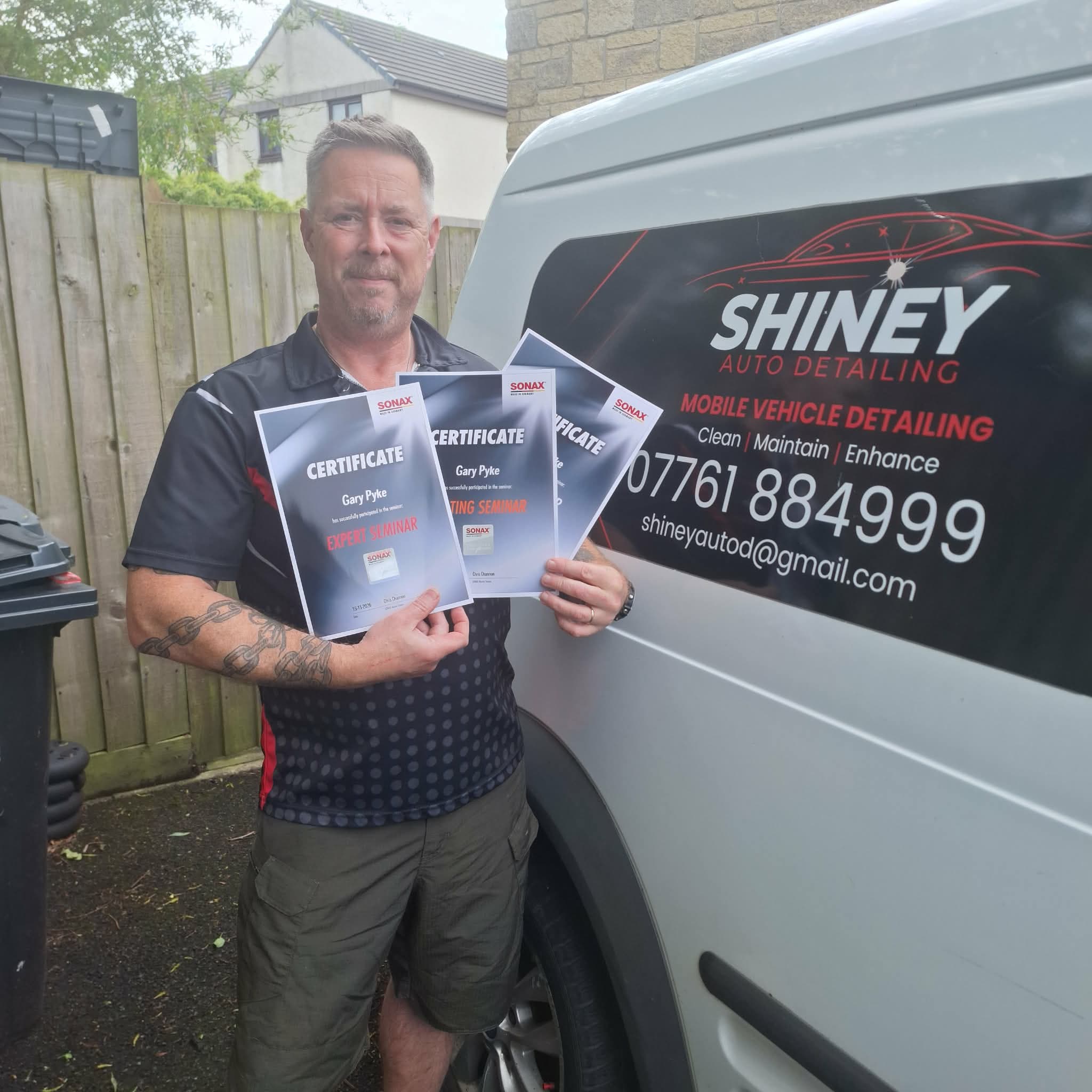 Gary, Shiney Auto Detailing owner, holding three SONAX detailer certificates beside his Shiney-branded van